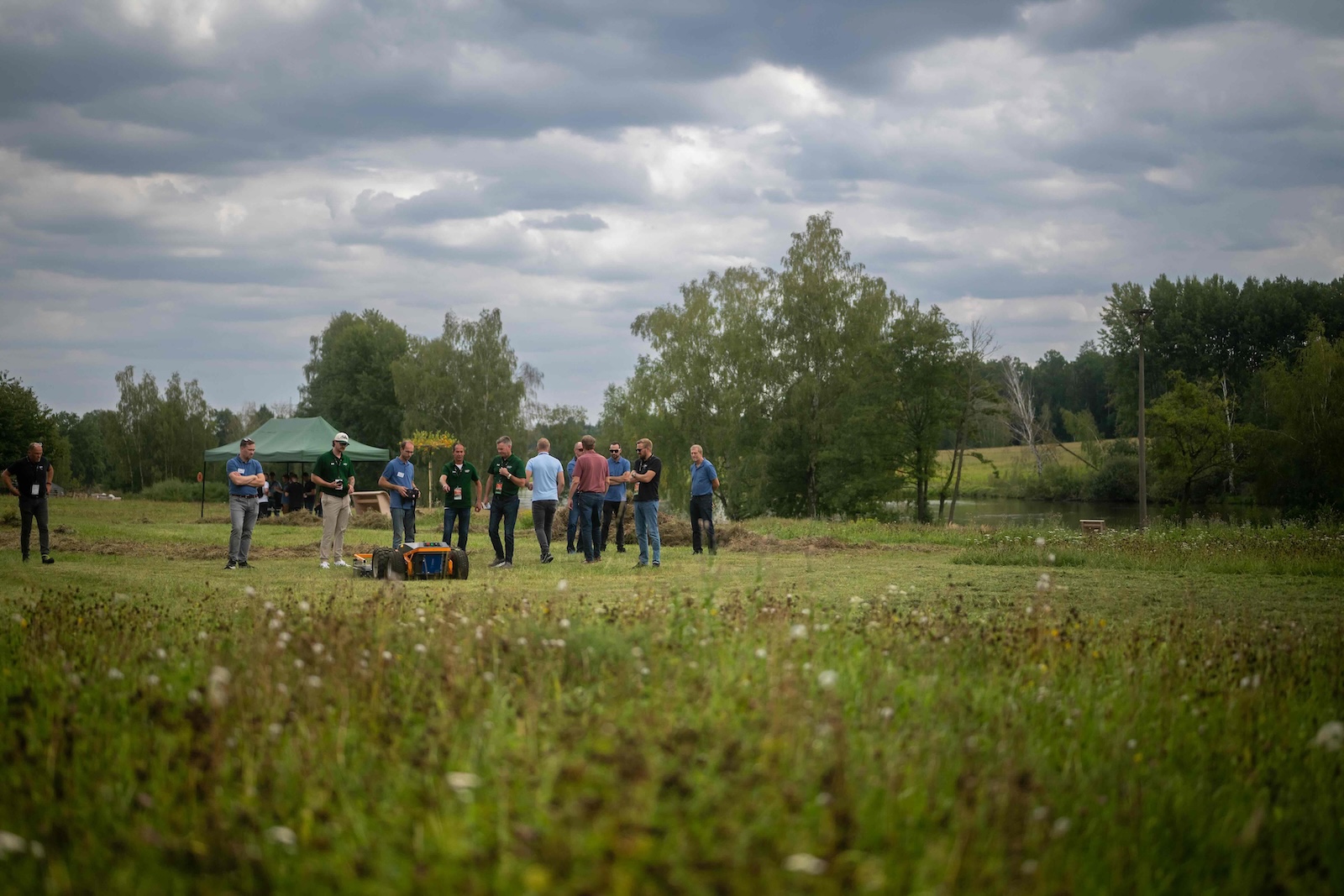 Wide shot of attendees around a robot with the pond and tent in the background