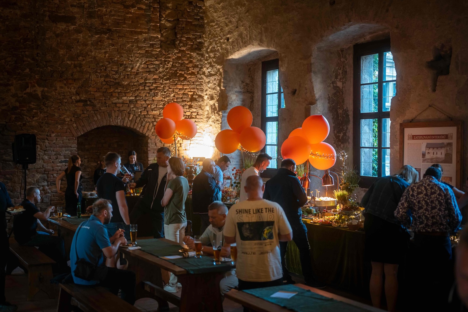 Guests dining under orange balloons in the vaulted castle hall