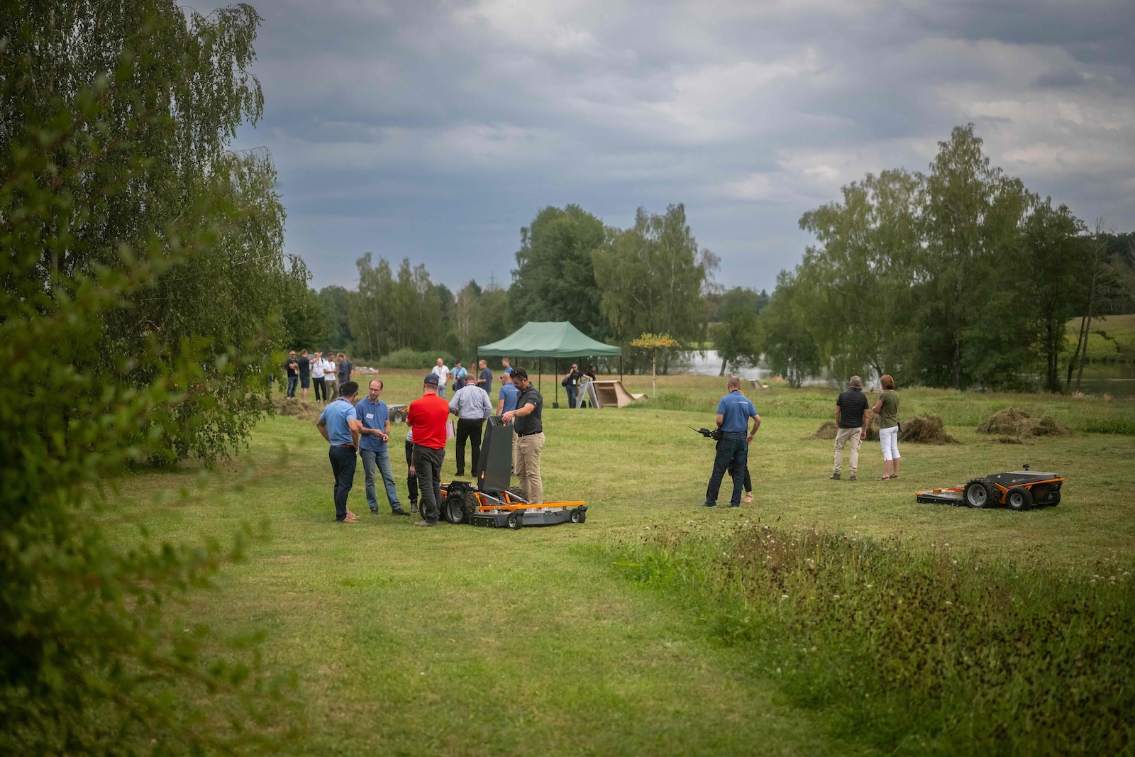 Wide view of the demo meadow with green tent, pond and groups of attendees