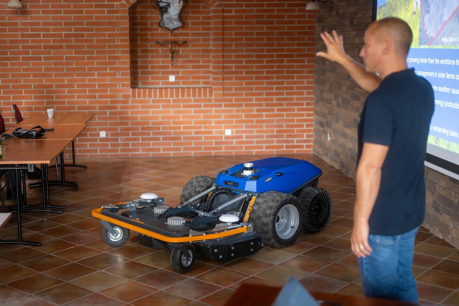 Blue Raymo robot with mowing deck presented indoors during the REDO Robotics talk