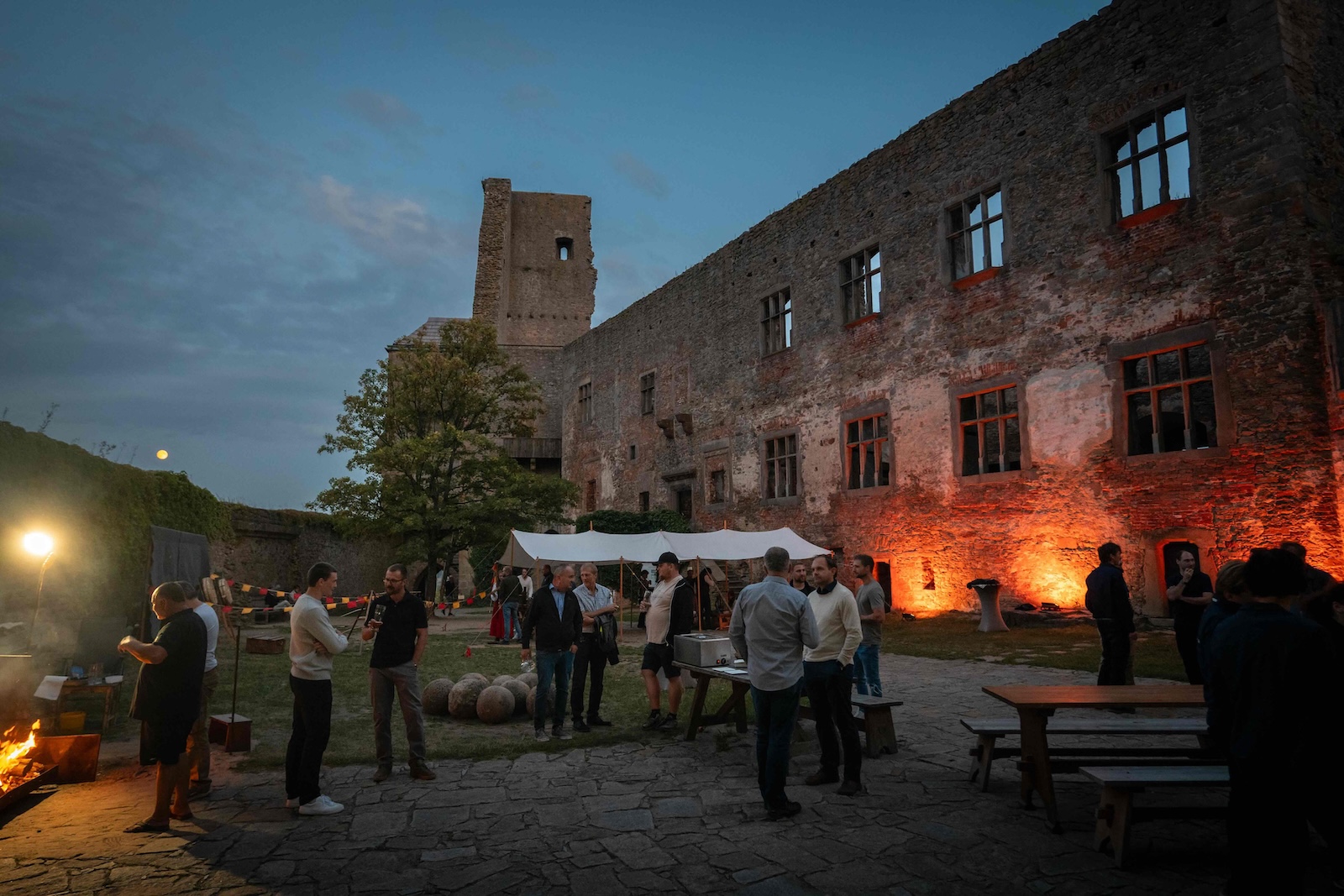 Attendees around the fire pit and tent in the castle courtyard at dusk