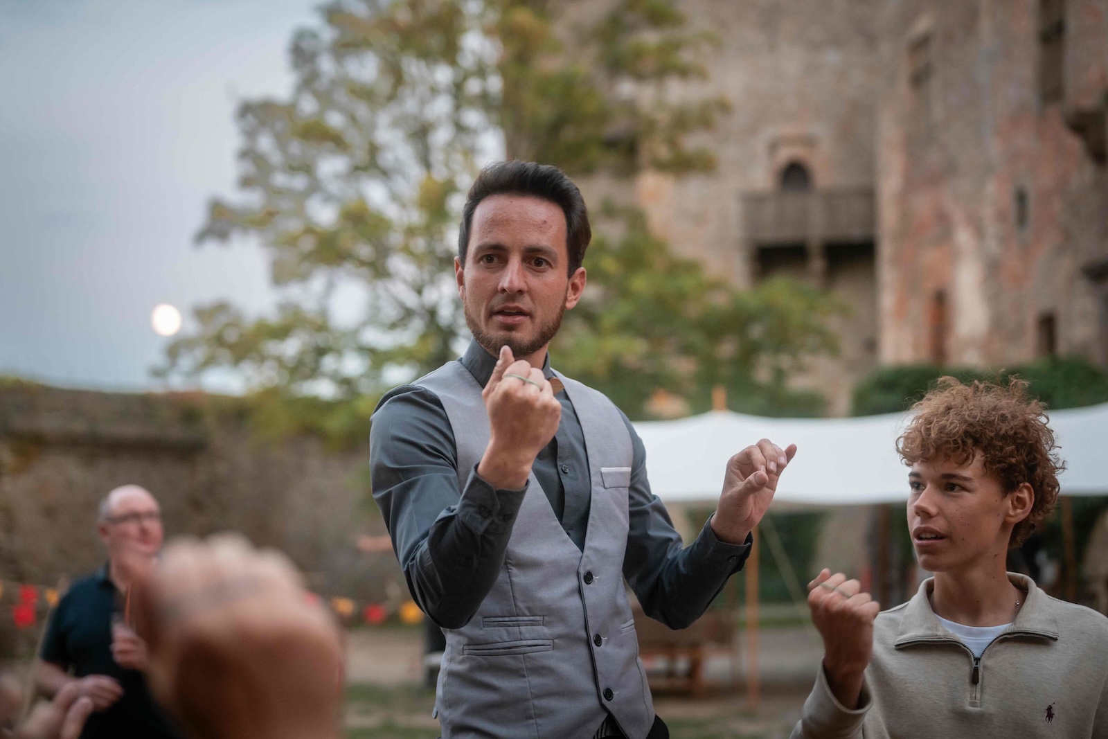 Host speaking energetically to guests in the castle courtyard at dusk