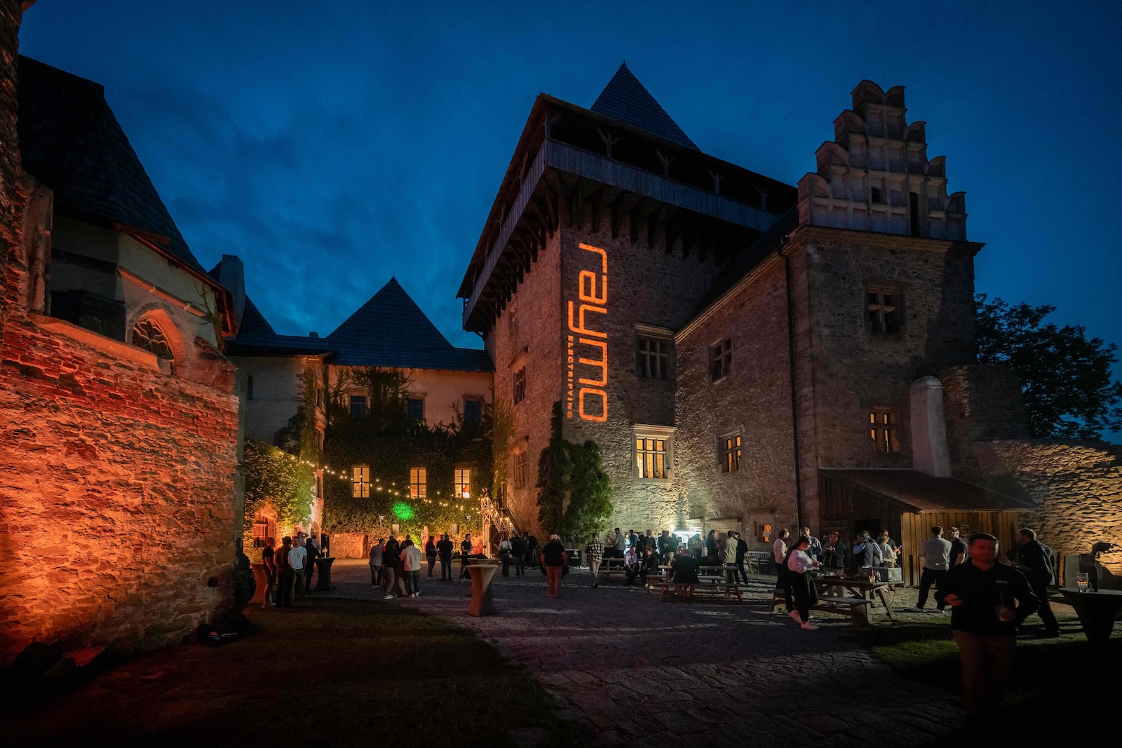 Guests in the castle courtyard under the illuminated Raymo sign
