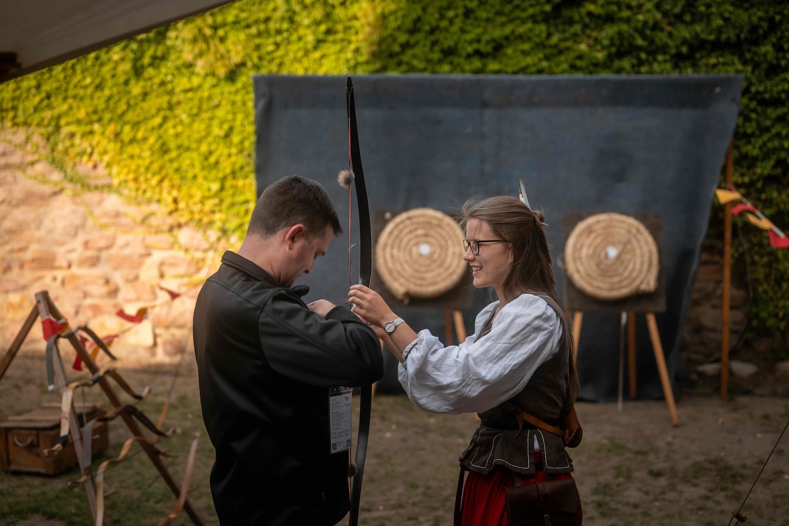 Costumed instructor handing a longbow to a guest at the archery range