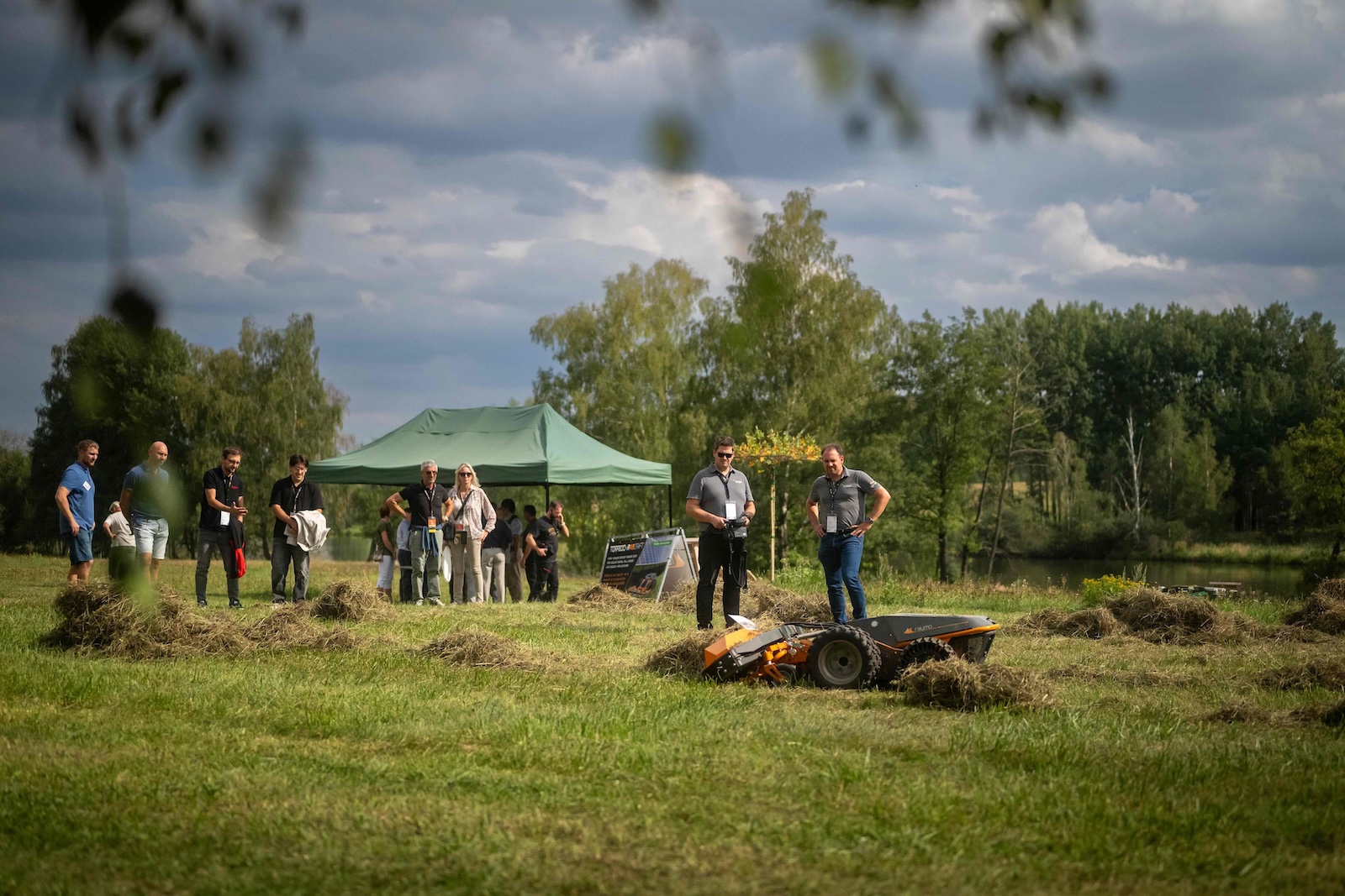 Operators controlling a Torpedo robot in freshly cut grass near the pond