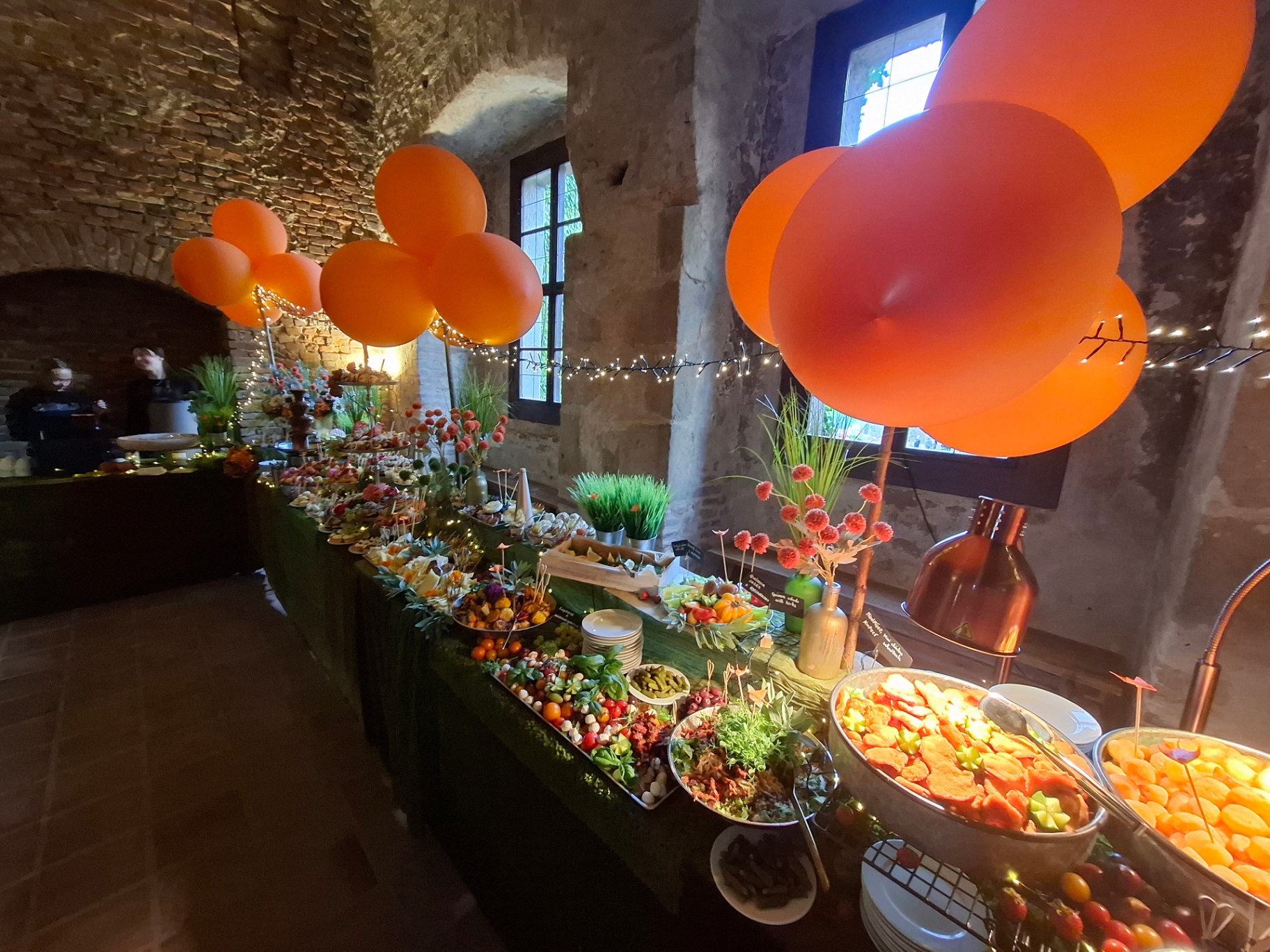 Buffet table with food and orange balloons in the vaulted hall