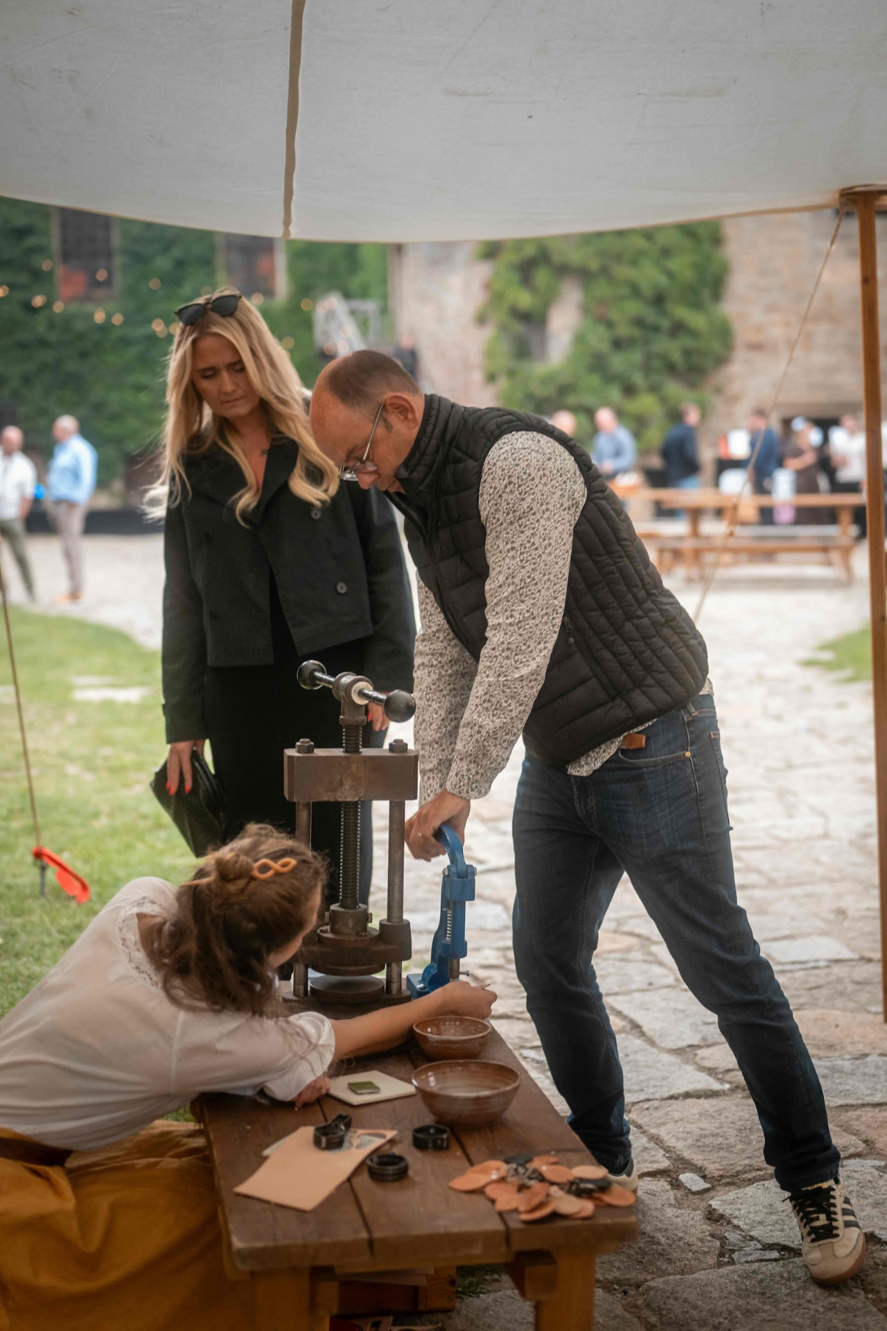 Couple watching the craftswoman press a leather token under the tent