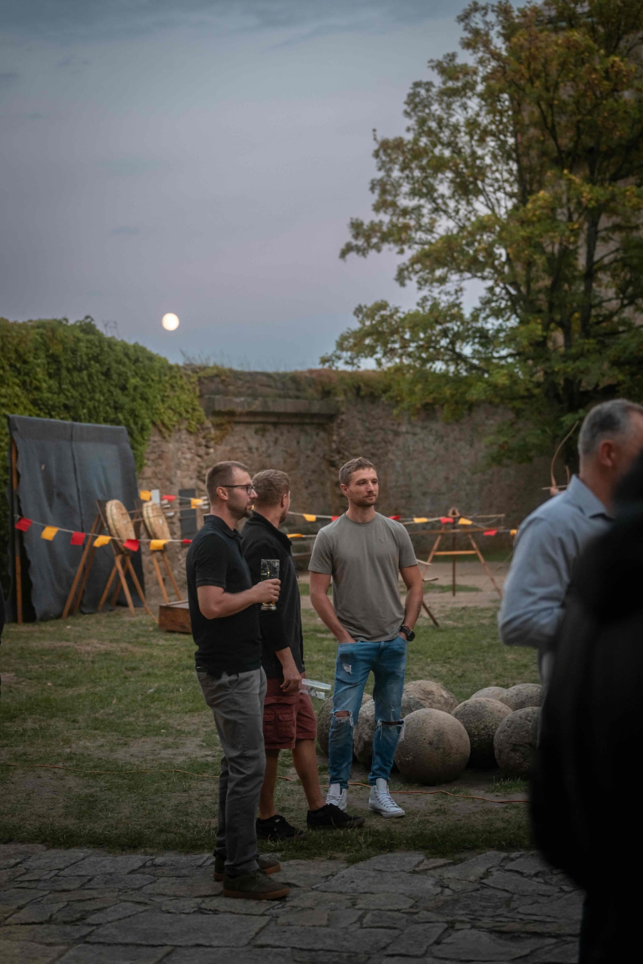 Attendees with drinks by the archery targets under the rising moon
