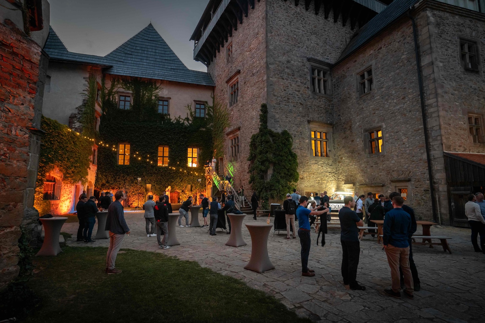 Castle courtyard at night with lit windows, bar and guests