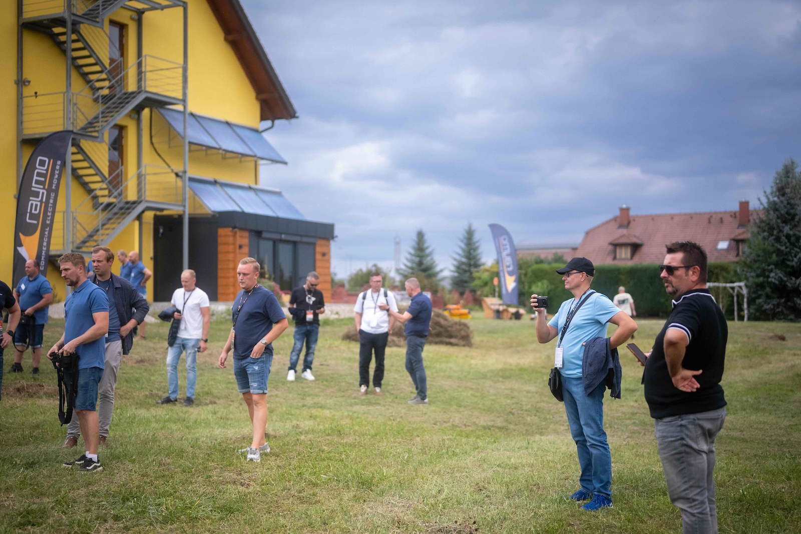 Attendees on the meadow in front of the yellow hotel building with Raymo flags