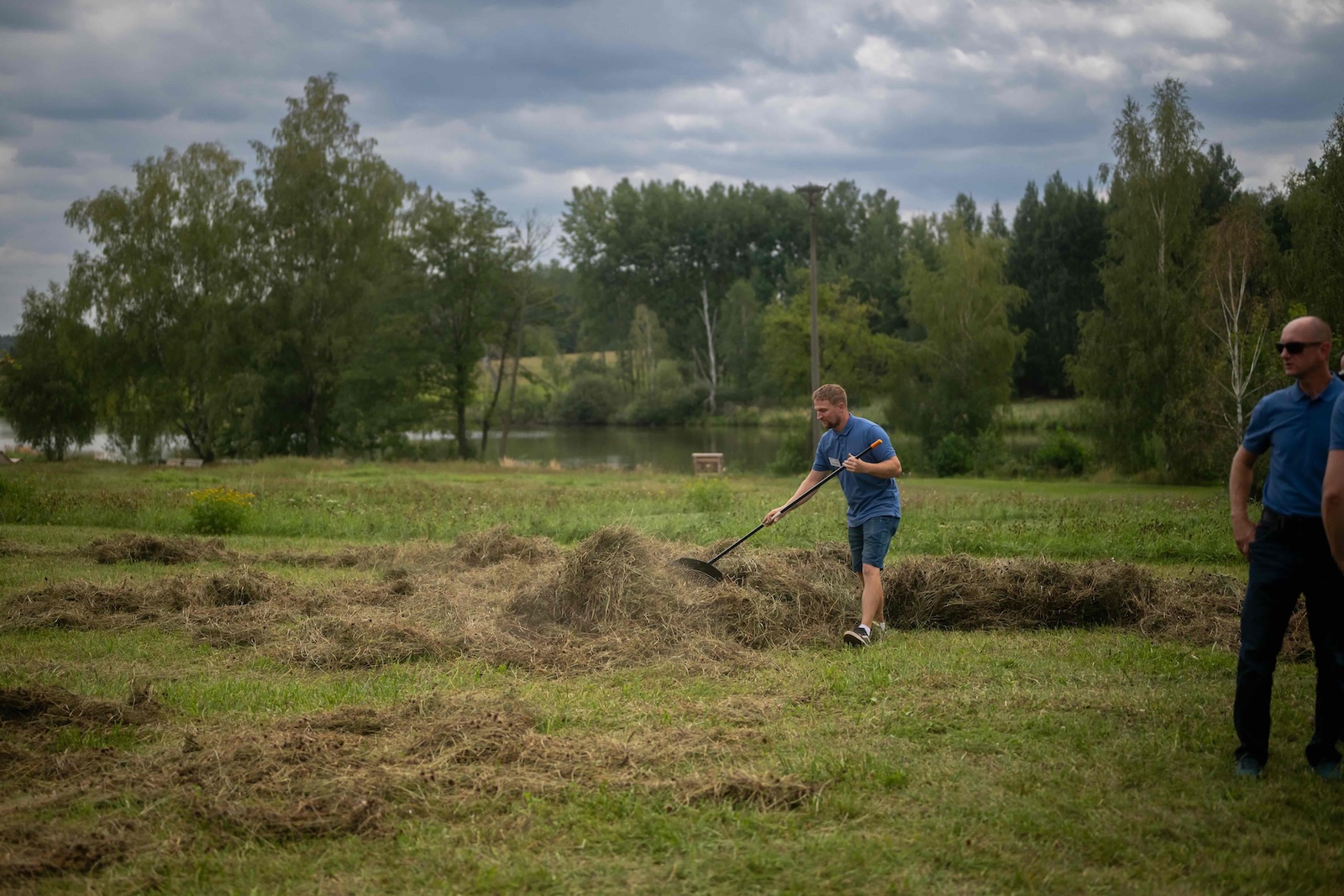 Team member raking cut grass on the demo meadow by the pond