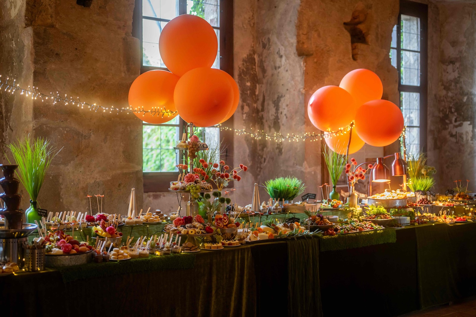 Festive buffet table with orange balloons and fairy lights in the castle hall