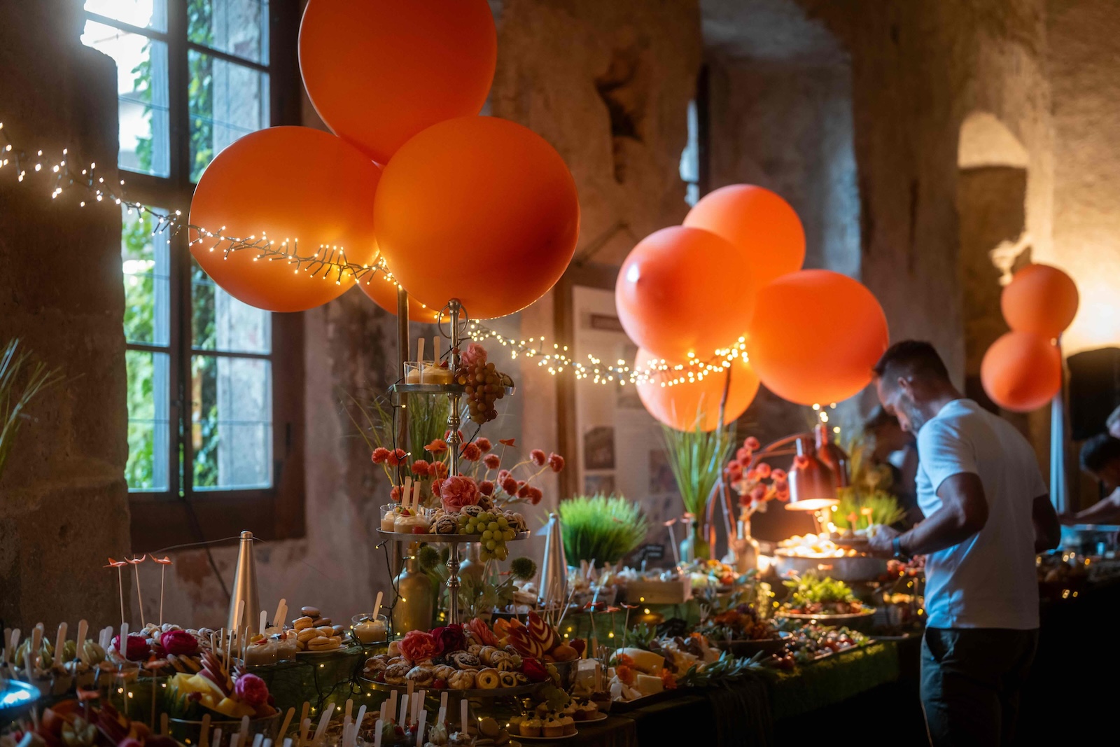 Buffet table with orange balloons and fairy lights in the castle hall