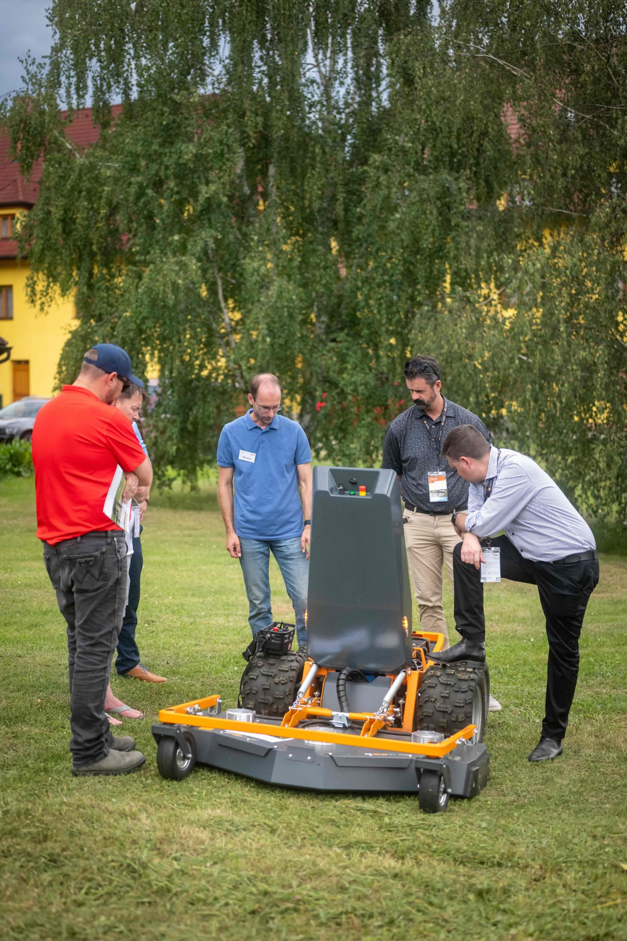 Group inspecting an orange Raymo carrier with a large mowing deck