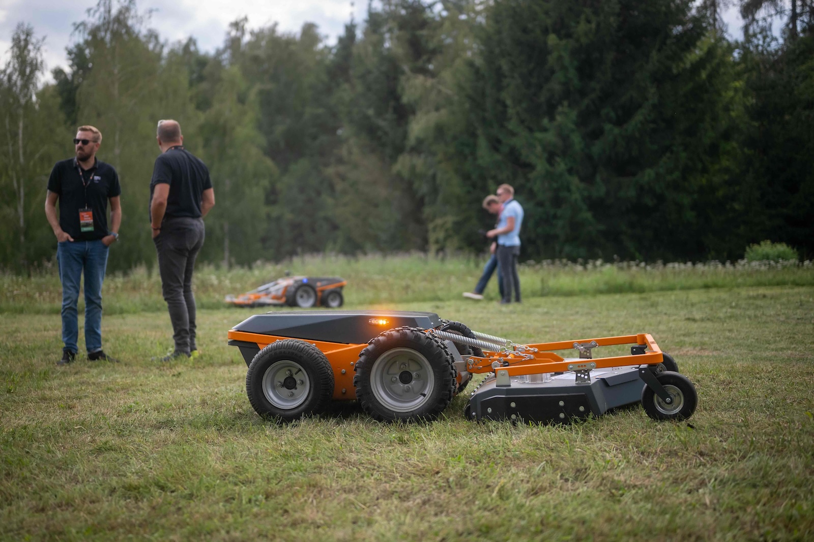 Orange Raymo carrier with rotary deck mowing while attendees watch