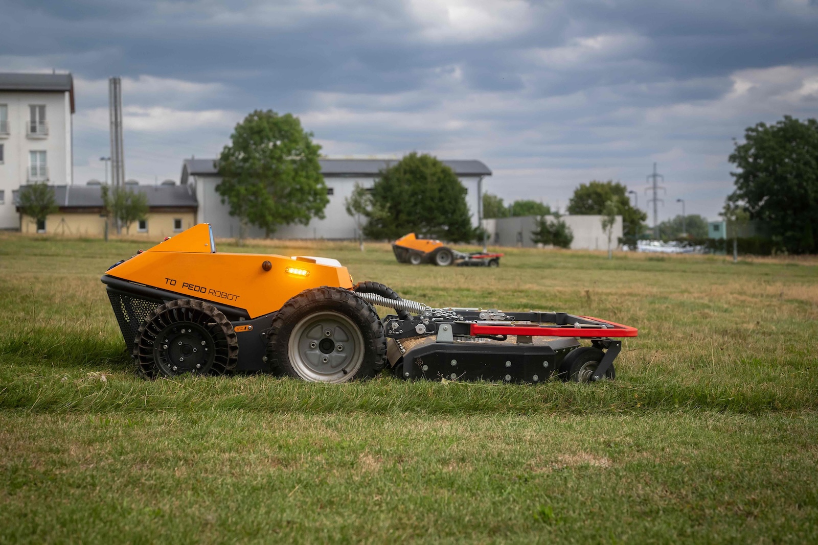 Orange Torpedo robot mowing the field with a second machine in the background