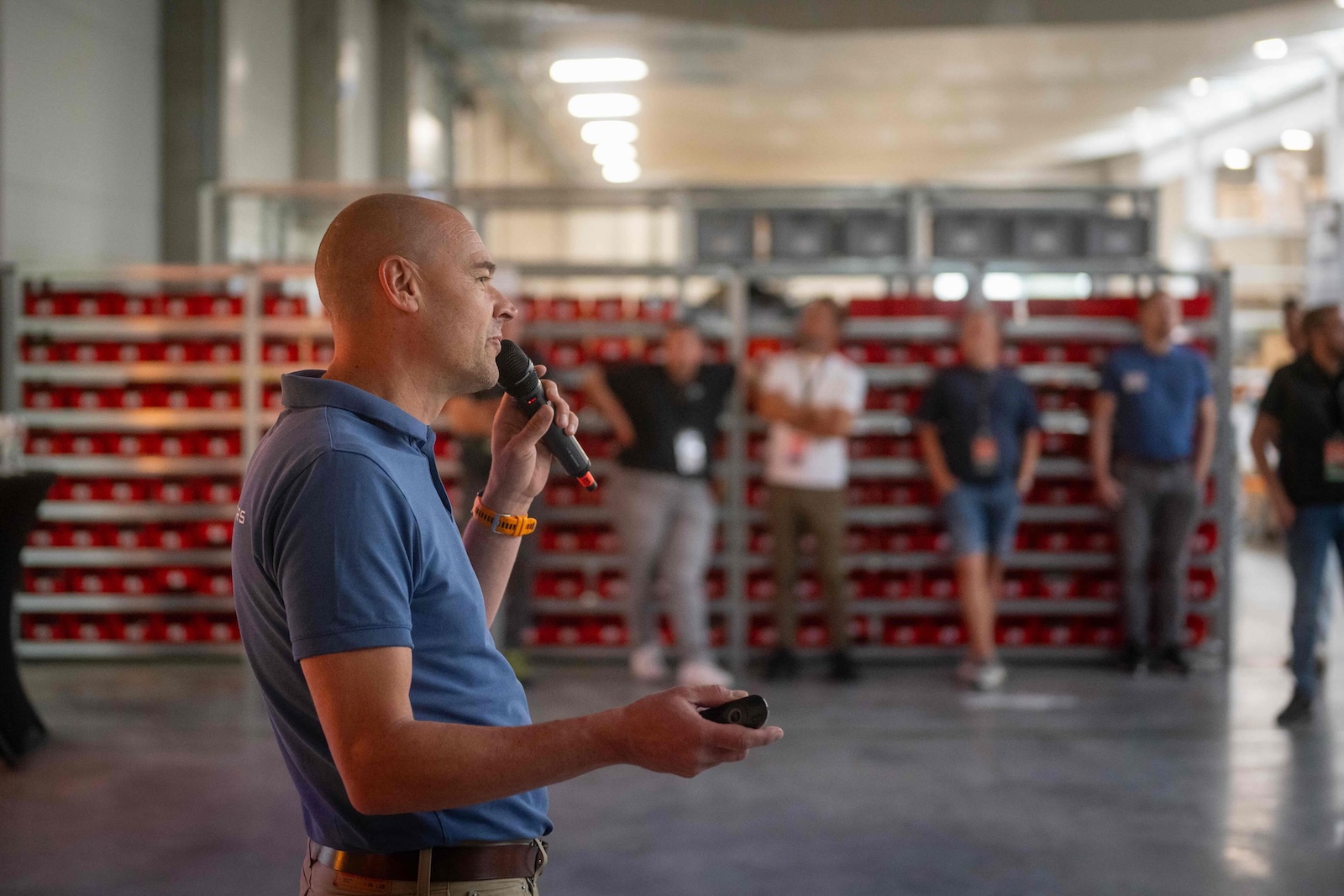 Speaker with a microphone presenting in front of the spare parts racks