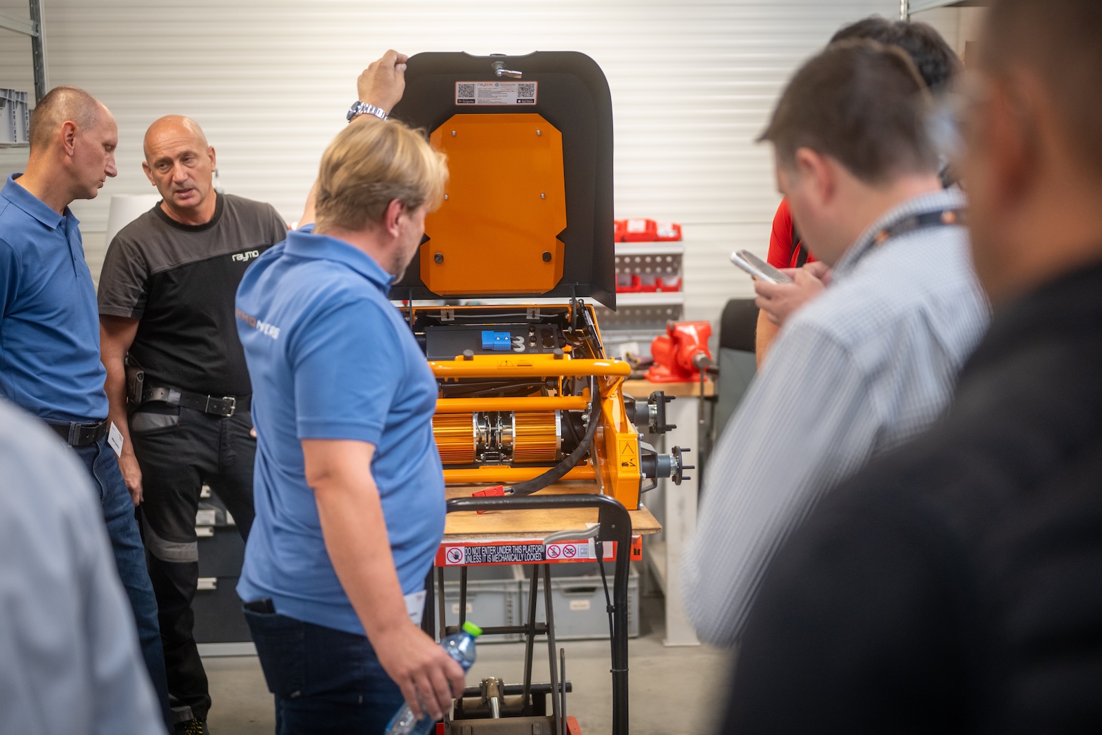Guests examining an opened orange mowing unit on a stand
