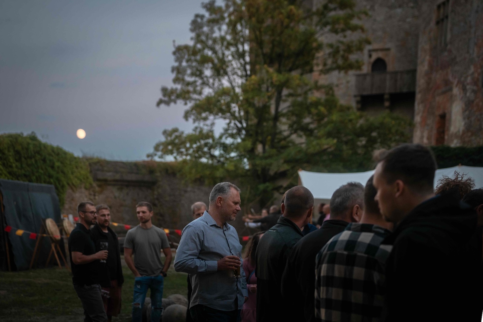 Guests talking in the courtyard as the full moon rises over the castle