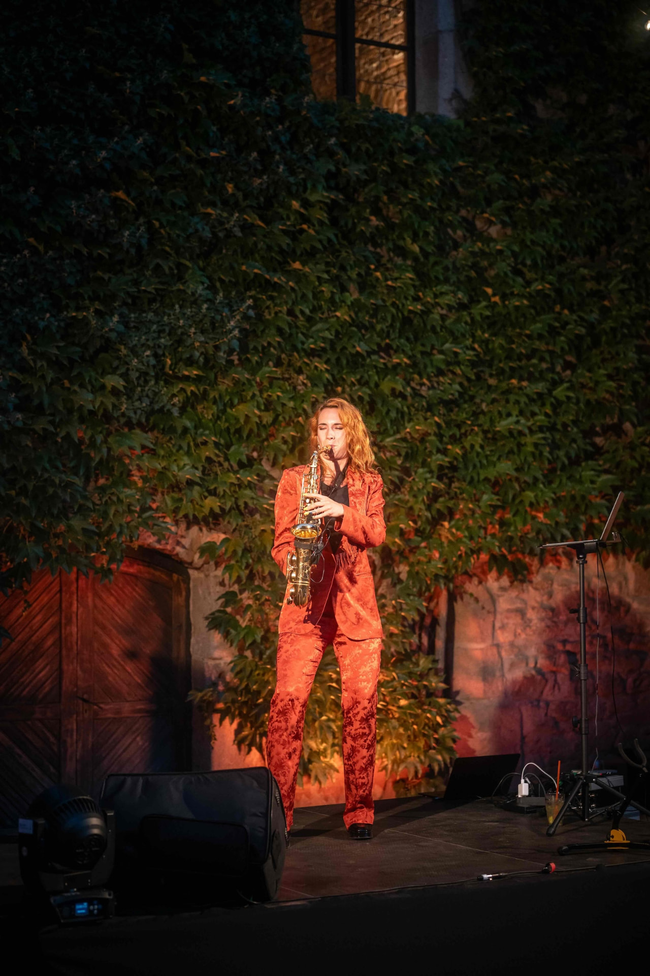 Saxophonist in a red suit performing on stage in front of the ivy wall